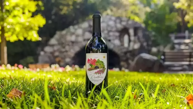 A dark wine bottle stands in green grass with the Grotto of visible in the background.